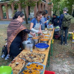 Eine lange Bierbank mit Broten mit veganem Aufstrich und anderem Essen wird von zwei Frauen verteilt
