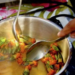 Ein Foto von einem Topf auf einer Heizplatte in dem Blüten ausgekocht werden, um darauf Pflanzenfarbe herzustellen. Zwei Hände rühren mit Löffeln im Topf.